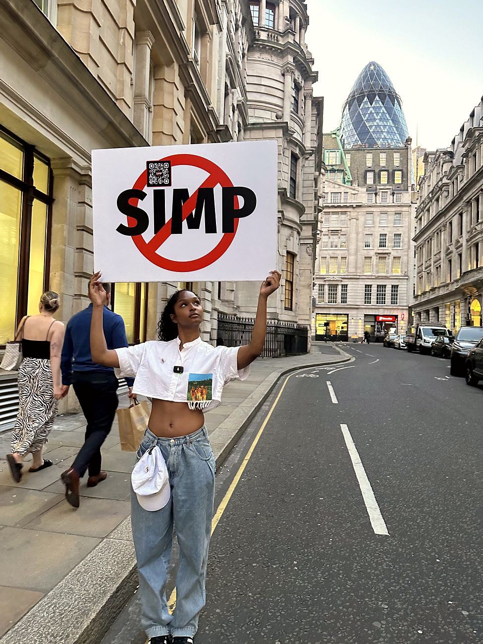 A woman holds a NO SIMP sign above her head on a City of London street