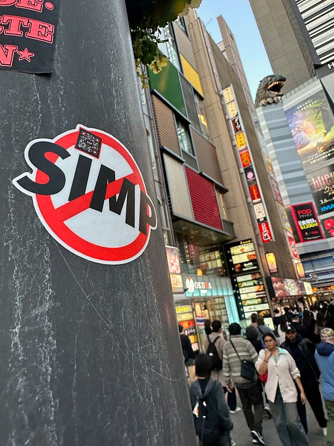 A NO SIMP sticker on a pillar in Shinjuku with the Godzilla head behind